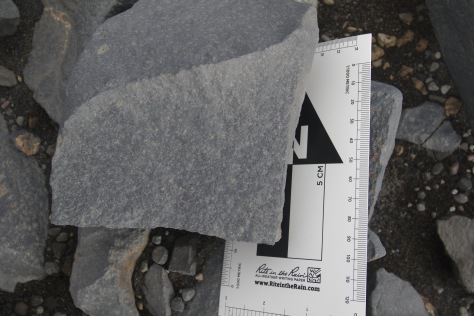 Float rock at Windy City.  The 1:1000 metric scale at right is effectively a mm scale.  Some olive/green crystals are visible, mostly 1-5 mm in their longest dimension, which are likely olivine (possibly clinopyroxene). Image credit: Bill Mitchell (CC-BY).