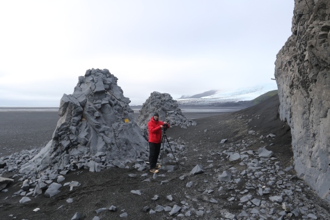 Looking eastward at Windy City, with a person for scale.  The gigapanned portion of the outcrop is at right, but two spires of similarly eroded rock outcrop further to the north of the photographed portion.  The stake coming out from the outcrop is a marker for one of our temperature/light intensity sensors. Image credit: Carlos Nascimento